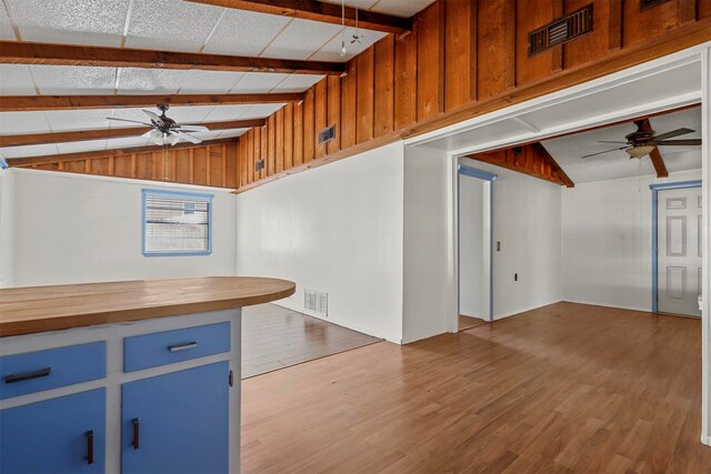 kitchen with wood walls, hardwood / wood-style floors, lofted ceiling with beams, and ceiling fan