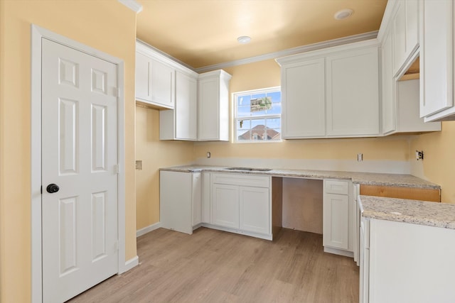 kitchen with white cabinetry, ornamental molding, light stone counters, and light wood-type flooring