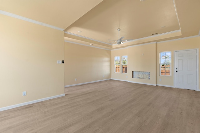 unfurnished living room with a tray ceiling, ornamental molding, ceiling fan, and light wood-type flooring