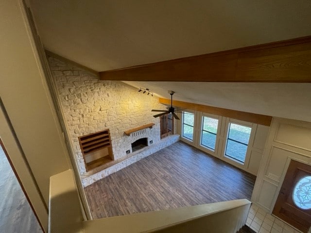 unfurnished living room with a fireplace, ceiling fan, light wood-type flooring, and vaulted ceiling with beams