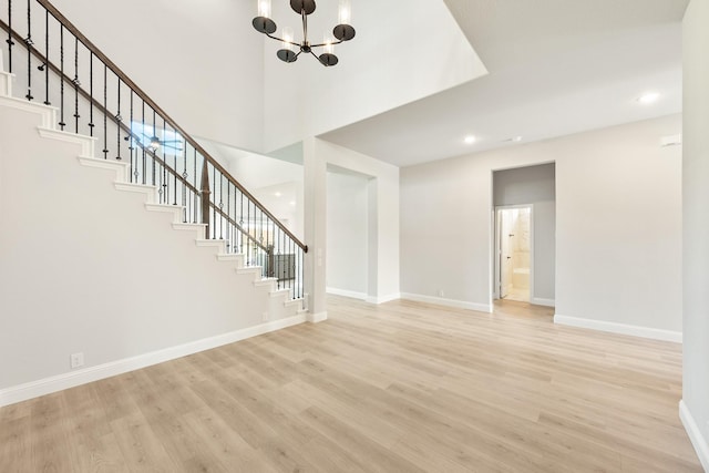 unfurnished living room featuring light hardwood / wood-style flooring, a chandelier, and a high ceiling