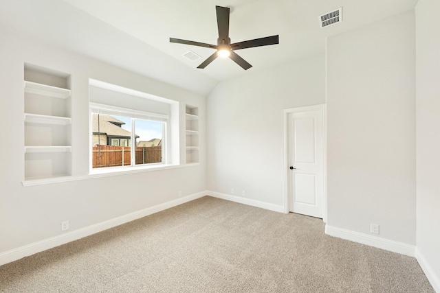 empty room with built in shelves, ceiling fan, carpet floors, and vaulted ceiling