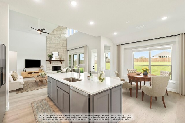 kitchen featuring gray cabinetry, a stone fireplace, sink, stainless steel dishwasher, and an island with sink