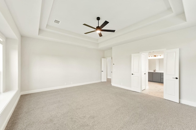 unfurnished bedroom featuring a raised ceiling, ceiling fan, and light carpet