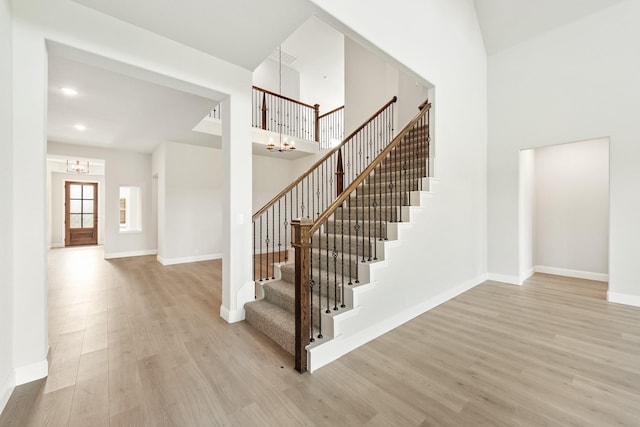 stairway with a chandelier, wood-type flooring, and a high ceiling