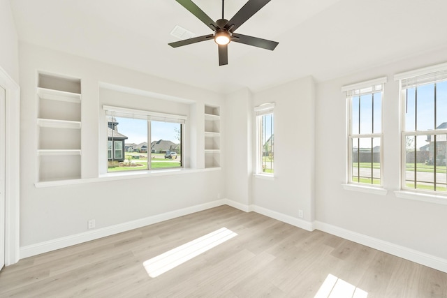 empty room with built in shelves, plenty of natural light, and light wood-type flooring