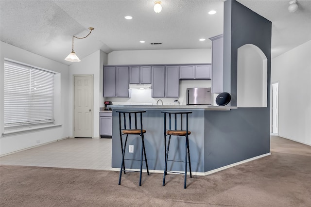 kitchen with a breakfast bar area, light colored carpet, decorative light fixtures, stainless steel fridge, and kitchen peninsula