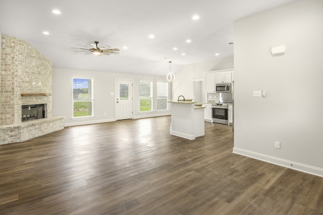 unfurnished living room featuring dark hardwood / wood-style floors, a fireplace, lofted ceiling, sink, and ceiling fan