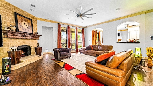 living room with ceiling fan, a fireplace, a textured ceiling, dark hardwood / wood-style flooring, and crown molding