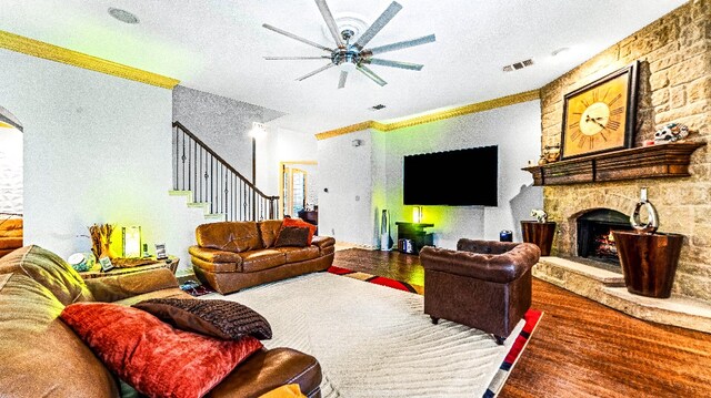 living room with ceiling fan, a stone fireplace, a textured ceiling, dark wood-type flooring, and ornamental molding