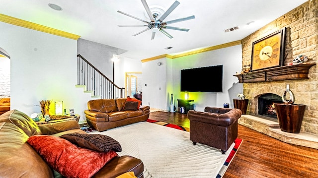 living room with ceiling fan, ornamental molding, dark wood-type flooring, and a stone fireplace