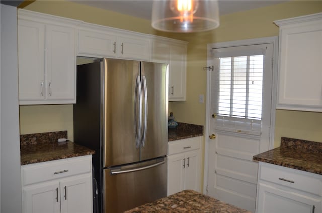 kitchen featuring dark stone countertops, stainless steel fridge, and white cabinetry