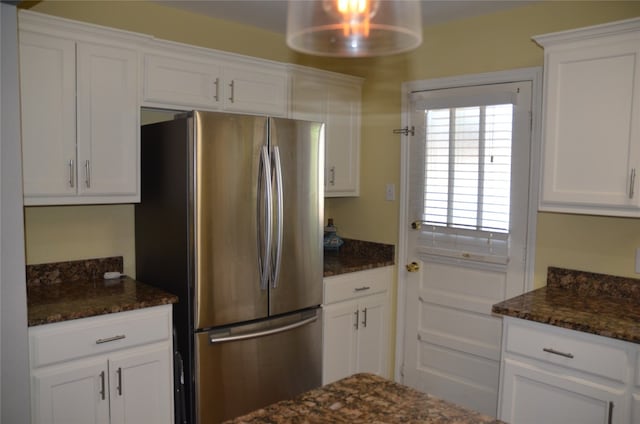 kitchen featuring dark stone countertops, stainless steel fridge, and white cabinetry