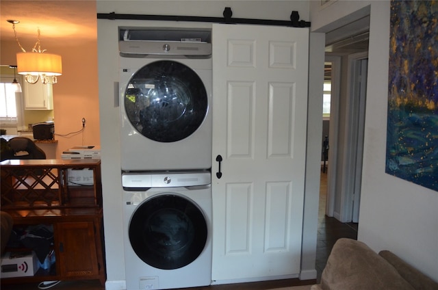 clothes washing area featuring dark tile floors, stacked washer and clothes dryer, and a barn door