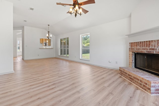 unfurnished living room with lofted ceiling, a brick fireplace, light hardwood / wood-style flooring, and ceiling fan with notable chandelier