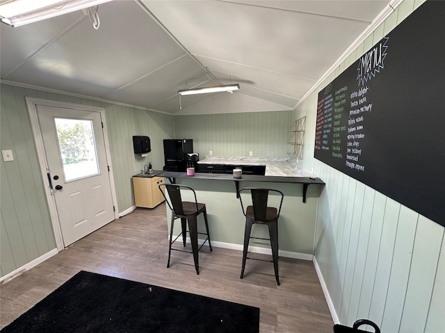 kitchen with lofted ceiling, crown molding, kitchen peninsula, hardwood / wood-style flooring, and a kitchen breakfast bar