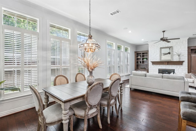 dining room featuring built in shelves, a stone fireplace, dark wood-type flooring, and ceiling fan with notable chandelier