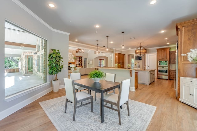 dining area with light hardwood / wood-style floors, a notable chandelier, ornamental molding, and sink