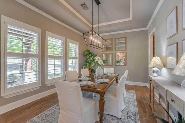 dining space featuring a notable chandelier, ornamental molding, a raised ceiling, and light wood-type flooring