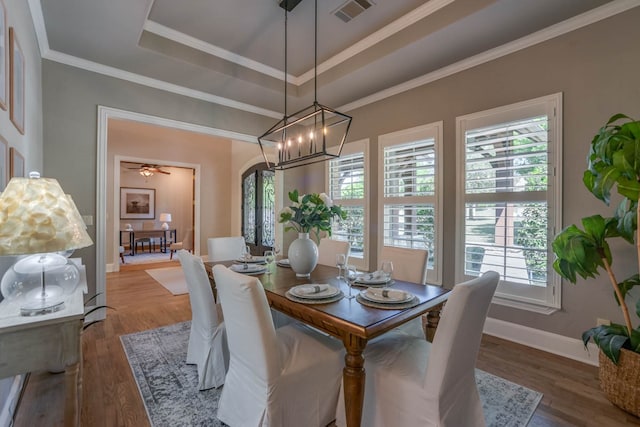 dining space with ornamental molding, hardwood / wood-style floors, ceiling fan with notable chandelier, and a raised ceiling