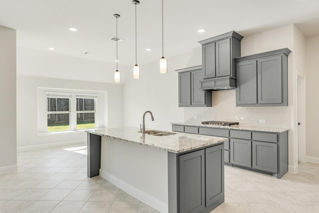 kitchen featuring pendant lighting, stainless steel gas stovetop, sink, gray cabinets, and light stone countertops