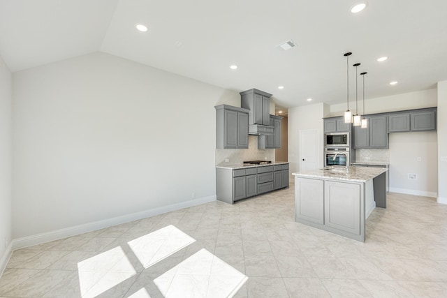 kitchen featuring lofted ceiling, backsplash, a center island with sink, gray cabinets, and appliances with stainless steel finishes