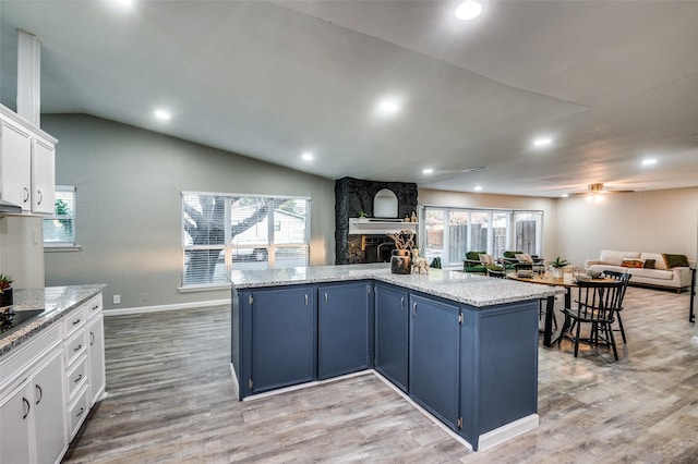 kitchen with white cabinetry, blue cabinets, a fireplace, light stone countertops, and a kitchen island