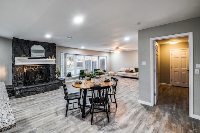 dining area featuring wood-type flooring, ceiling fan, and a fireplace