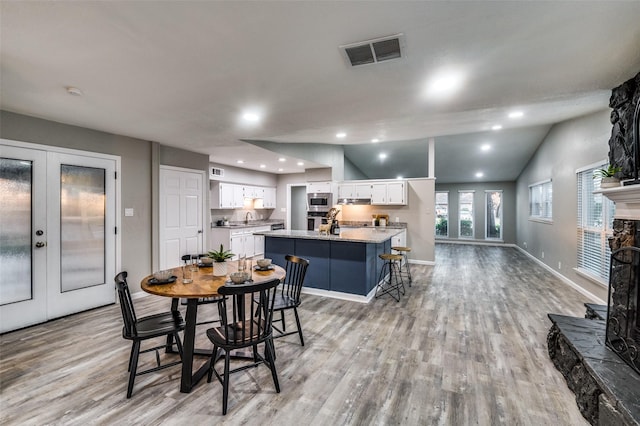 dining space with french doors, a stone fireplace, sink, vaulted ceiling, and light wood-type flooring