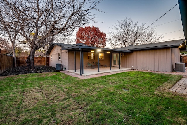 back house at dusk with a yard, central AC, and a patio area