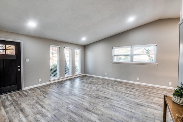 entrance foyer featuring lofted ceiling, a textured ceiling, and light hardwood / wood-style flooring