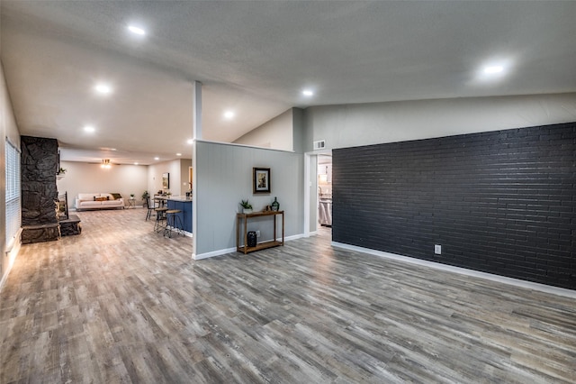 living room featuring brick wall, lofted ceiling, and hardwood / wood-style floors