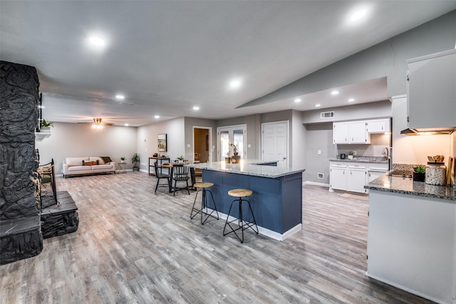 kitchen featuring white cabinetry, a kitchen island, light stone counters, and light hardwood / wood-style flooring