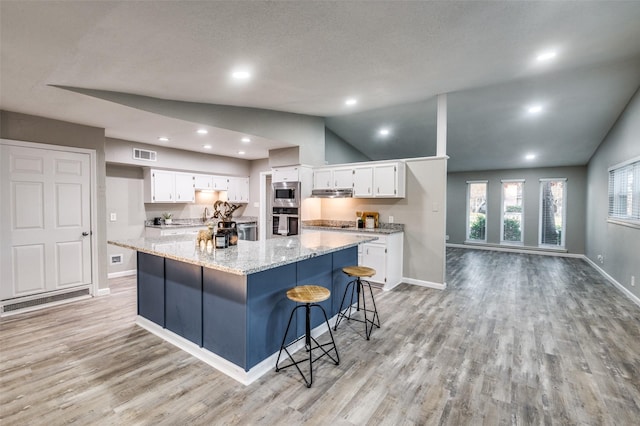 kitchen with appliances with stainless steel finishes, a spacious island, light stone counters, white cabinets, and vaulted ceiling