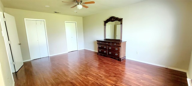 unfurnished bedroom with ceiling fan, dark hardwood / wood-style floors, and multiple closets