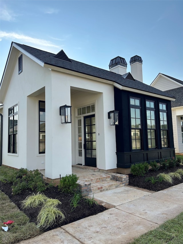 exterior space featuring stucco siding, roof with shingles, and a chimney