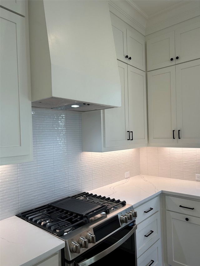 kitchen featuring backsplash, white cabinets, gas stove, and wall chimney exhaust hood