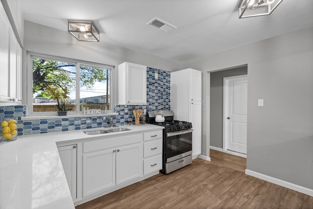 kitchen featuring stainless steel gas range, white cabinets, sink, light hardwood / wood-style floors, and tasteful backsplash