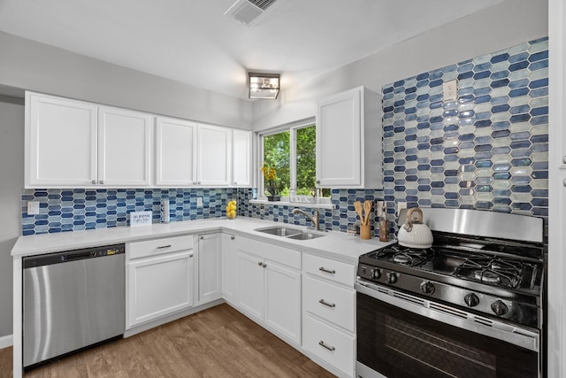 kitchen featuring appliances with stainless steel finishes, white cabinets, sink, tasteful backsplash, and light wood-type flooring