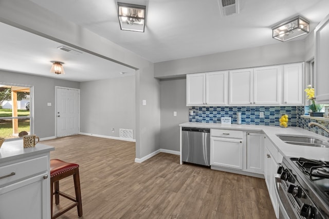 kitchen with appliances with stainless steel finishes, sink, tasteful backsplash, light wood-type flooring, and white cabinetry