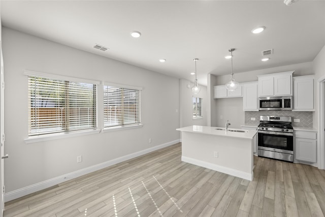 kitchen featuring white cabinets, pendant lighting, appliances with stainless steel finishes, and light hardwood / wood-style flooring