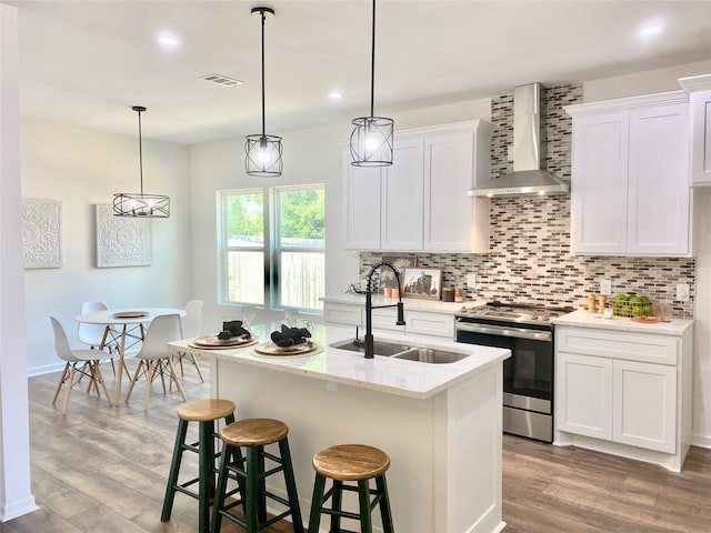 kitchen featuring light hardwood / wood-style flooring, stainless steel stove, sink, backsplash, and wall chimney exhaust hood