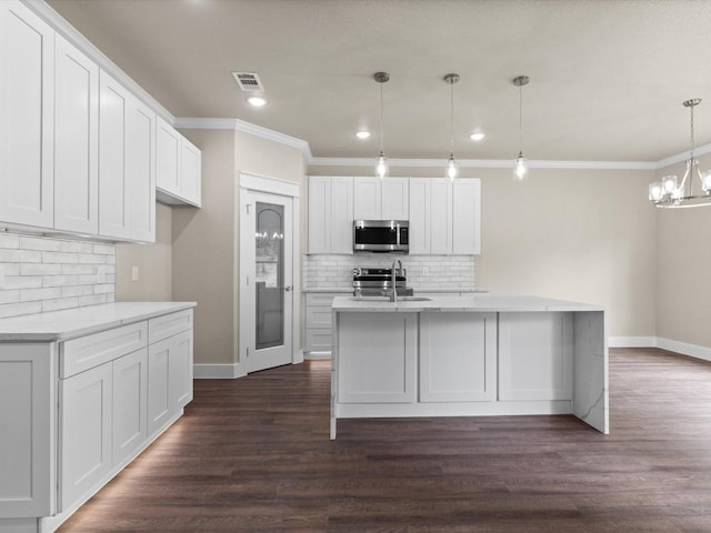 kitchen with decorative light fixtures, backsplash, stainless steel appliances, white cabinetry, and dark hardwood / wood-style flooring