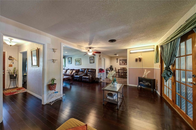 living room with ceiling fan, a wood stove, dark wood-type flooring, and a textured ceiling