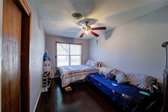 bedroom with ceiling fan, dark wood-type flooring, and a textured ceiling