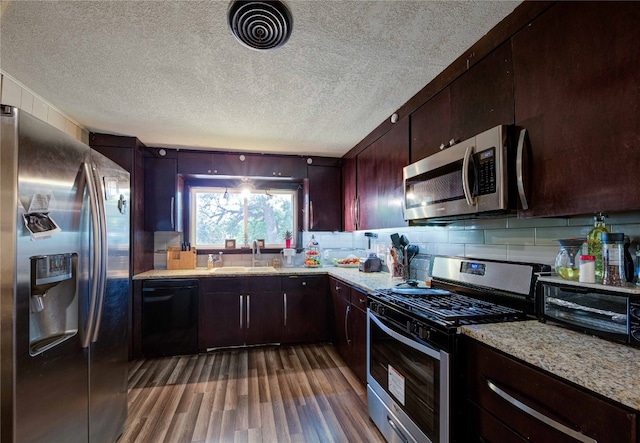 kitchen featuring dark hardwood / wood-style floors, appliances with stainless steel finishes, light stone counters, tasteful backsplash, and dark brown cabinetry