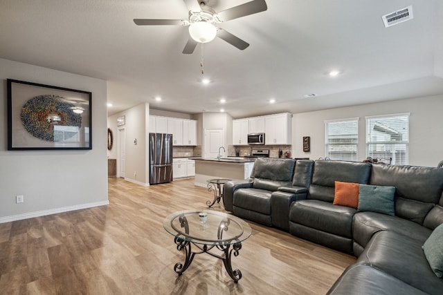 living room with light hardwood / wood-style flooring, ceiling fan, and sink