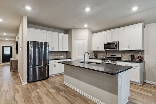 kitchen with light hardwood / wood-style floors, stainless steel appliances, white cabinetry, and an island with sink