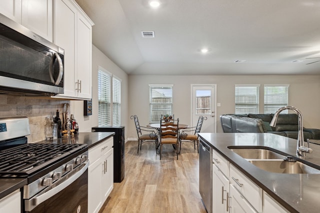 kitchen with white cabinets, sink, backsplash, stainless steel appliances, and light hardwood / wood-style flooring