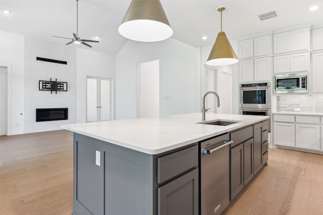 kitchen featuring decorative backsplash, light wood-type flooring, sink, white cabinetry, and stainless steel microwave